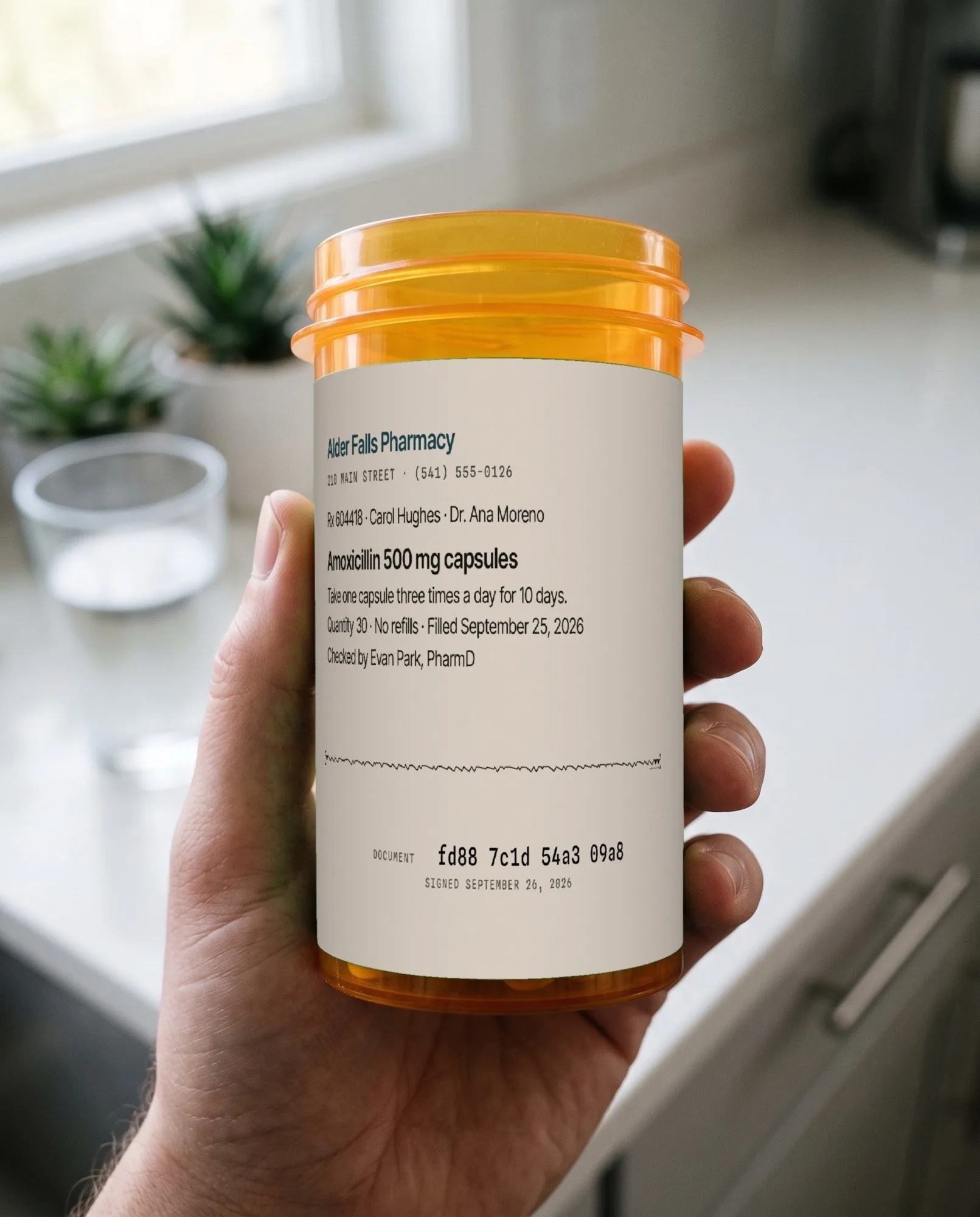 In a kitchen, a hand holds an amber prescription bottle. The white label carries a wavy mark and its code.